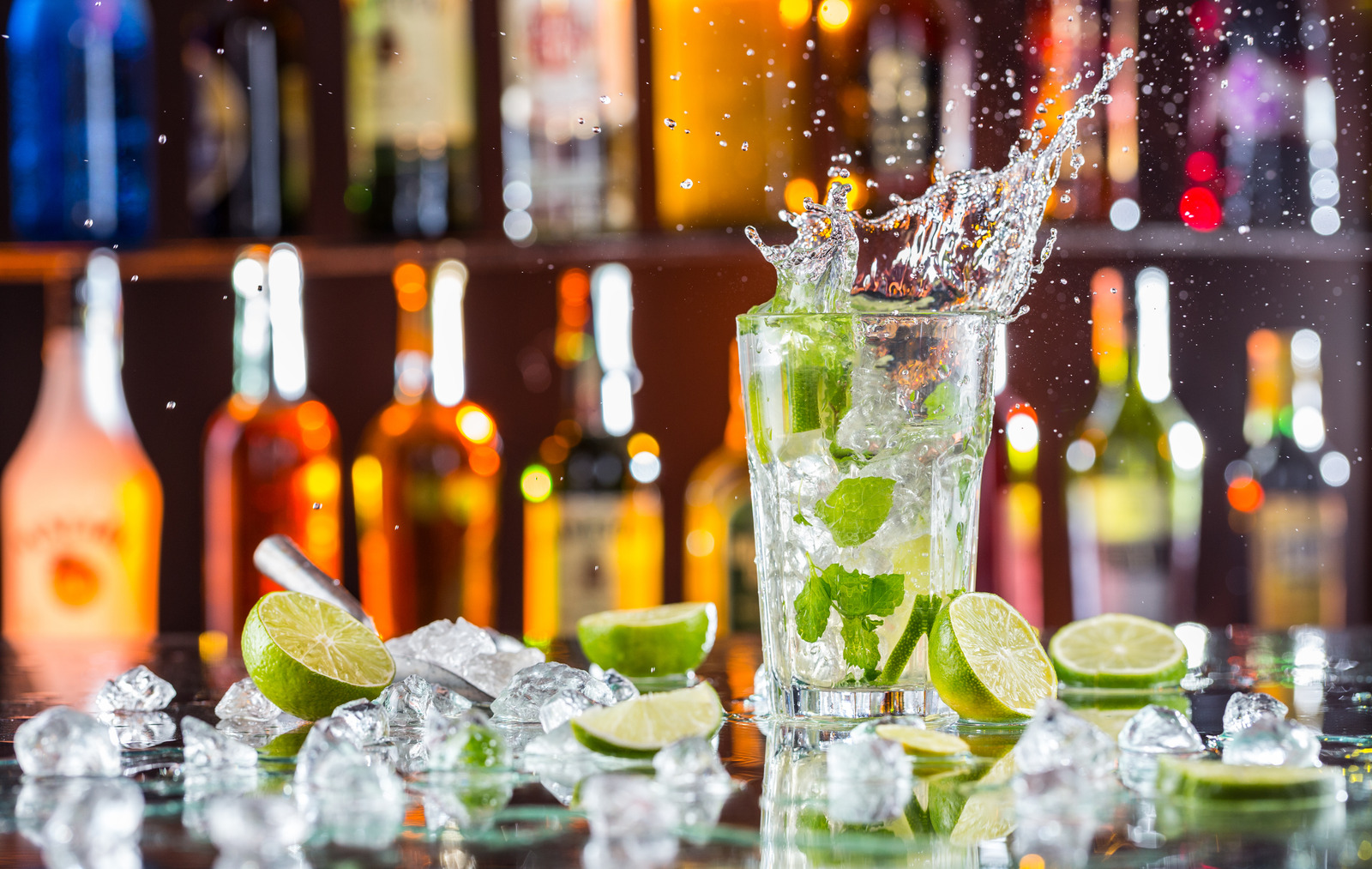 Mojito cocktail drink with splash, served on bar counter with blur bottles on background