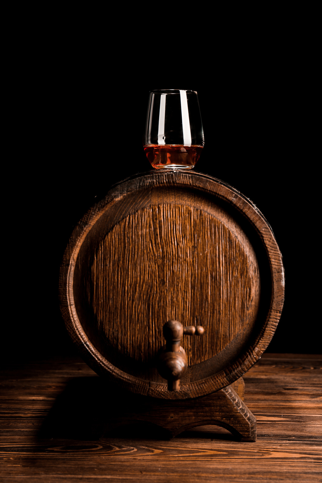 Glass of whiskey on wooden barrel against black background